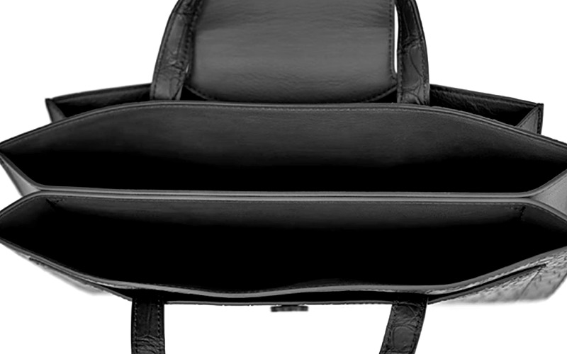 Open black leather handbag viewed from above, showing two main compartments and empty dark interior lining.